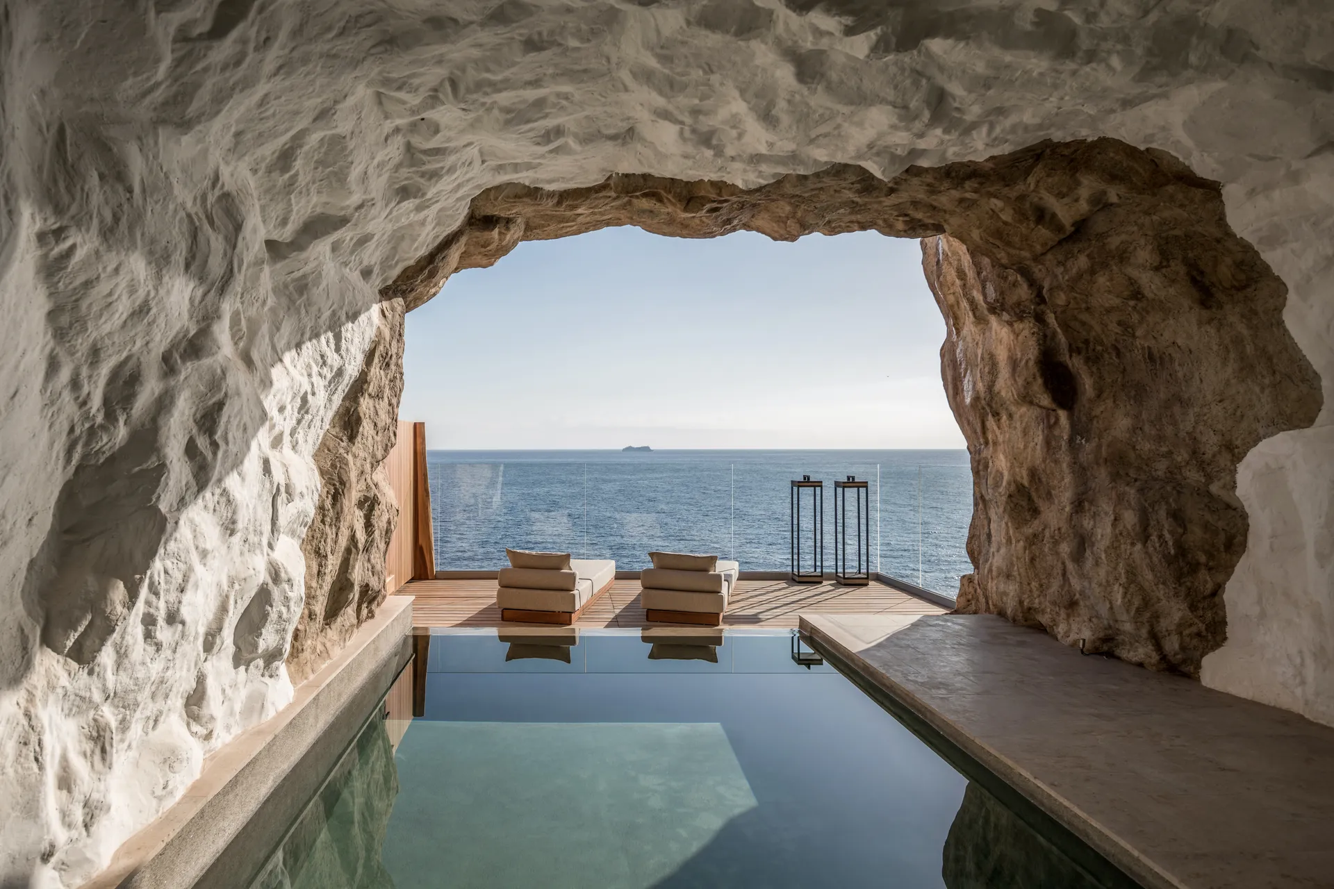 Interior of a Cave Suite at Acro Suites, featuring stone walls and expansive glass windows with sea views.