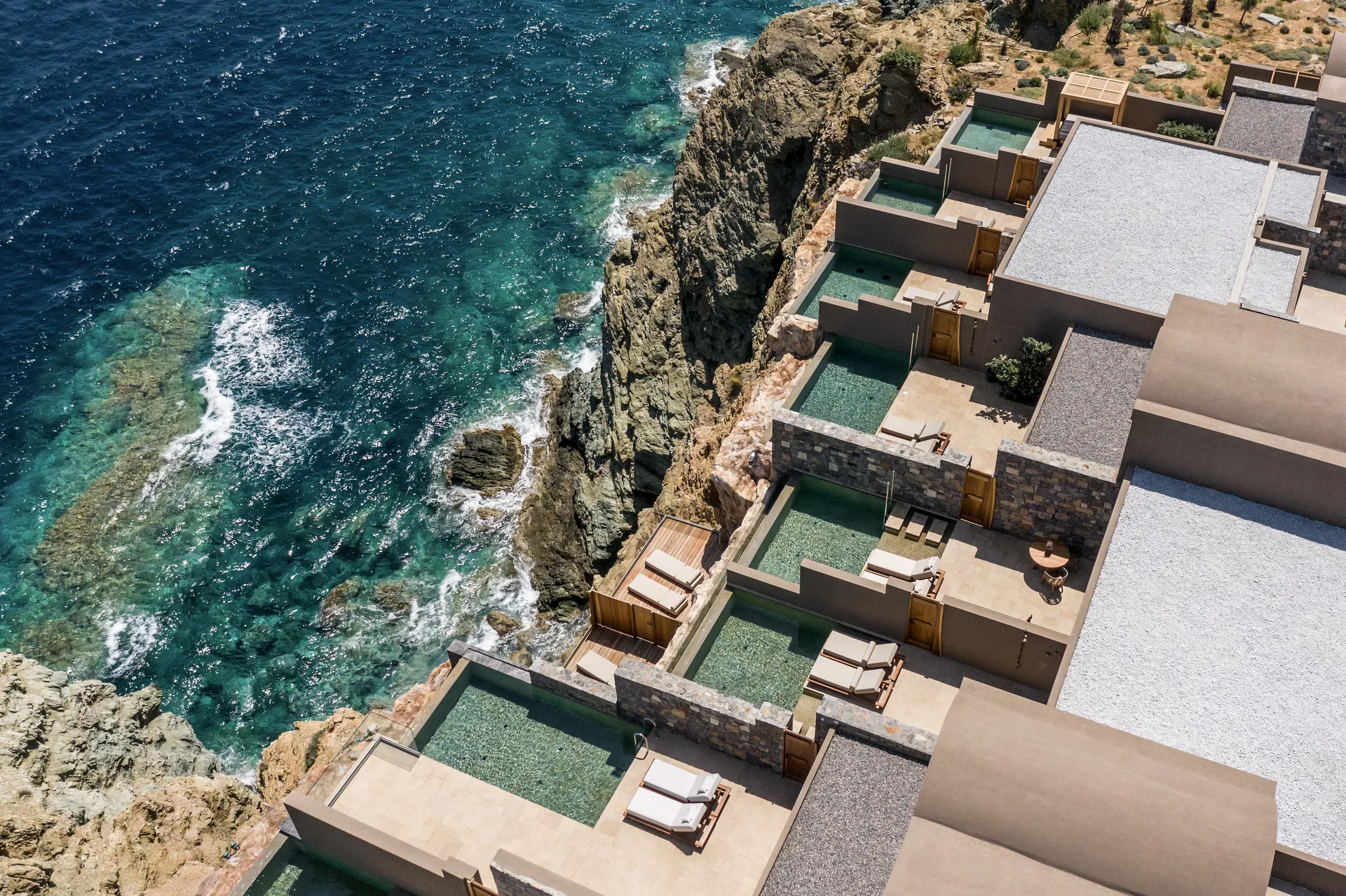 Aerial view of Acro Suites perched on the cliffs of Crete with the Aegean Sea in the background.