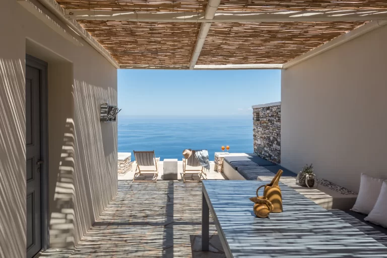 Shaded outdoor dining area at Verina Astra with natural wood furniture and a backdrop of the Aegean.